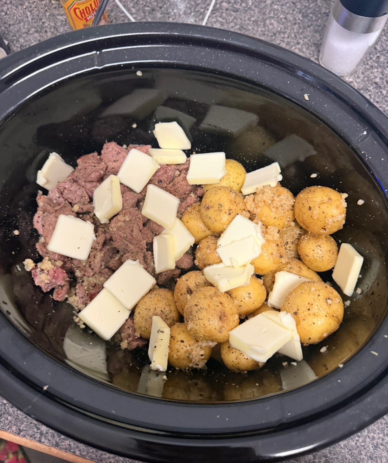 Raw beef stew meat and mini potatoes with butter pats in a slow cooker before cooking