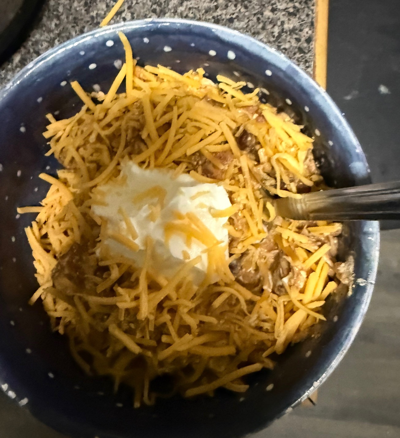 Crock Pot Cream Cheese Chicken Chili in a bowl topped with shredded cheese and a dollop of sour cream